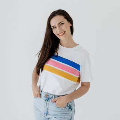 A young mum  modelling a white nursing shirt that features three colored stripes, blue, pink and yellow.