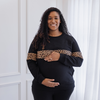 A pregnant woman wearing a nursing sweater and cradling her bump.