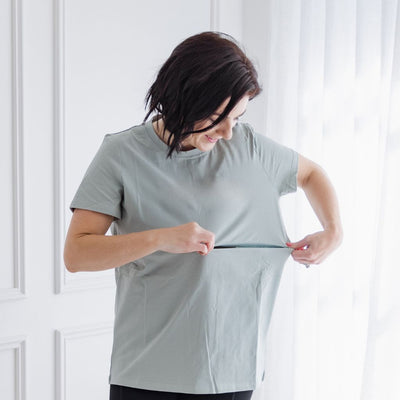 A petite woman shows a hidden zip in a sage nursing t-shirt.