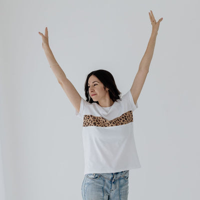 A young mum raising her hands in celebration while wearing a white and leopard print breastfeeding top.