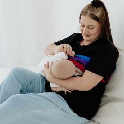 A young mum smiling down at her baby as she breastfeeds easily with a black nursing t-shirt.