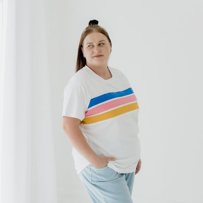 A size 16 mum modelling a white nursing tee that has coloured stripes.