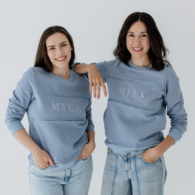 Two young mums wearing steel blue jumpers that feature the word MYLK embroidered on the chest.