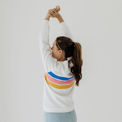 A young mum stretches her hands up high to show the length of a white breastfeeding jumper.