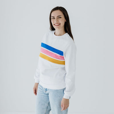 A young woman smiles as she wears a white nursing jumper with three coloured panels in blue, pink and yellow.