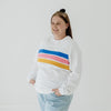 A size XL woman wearing a white nursing jumper that has three stripes in blue, pink and yellow.