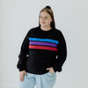 A XL woman wearing a black nursing jumper with three coloured stripes, blue, purple and red.